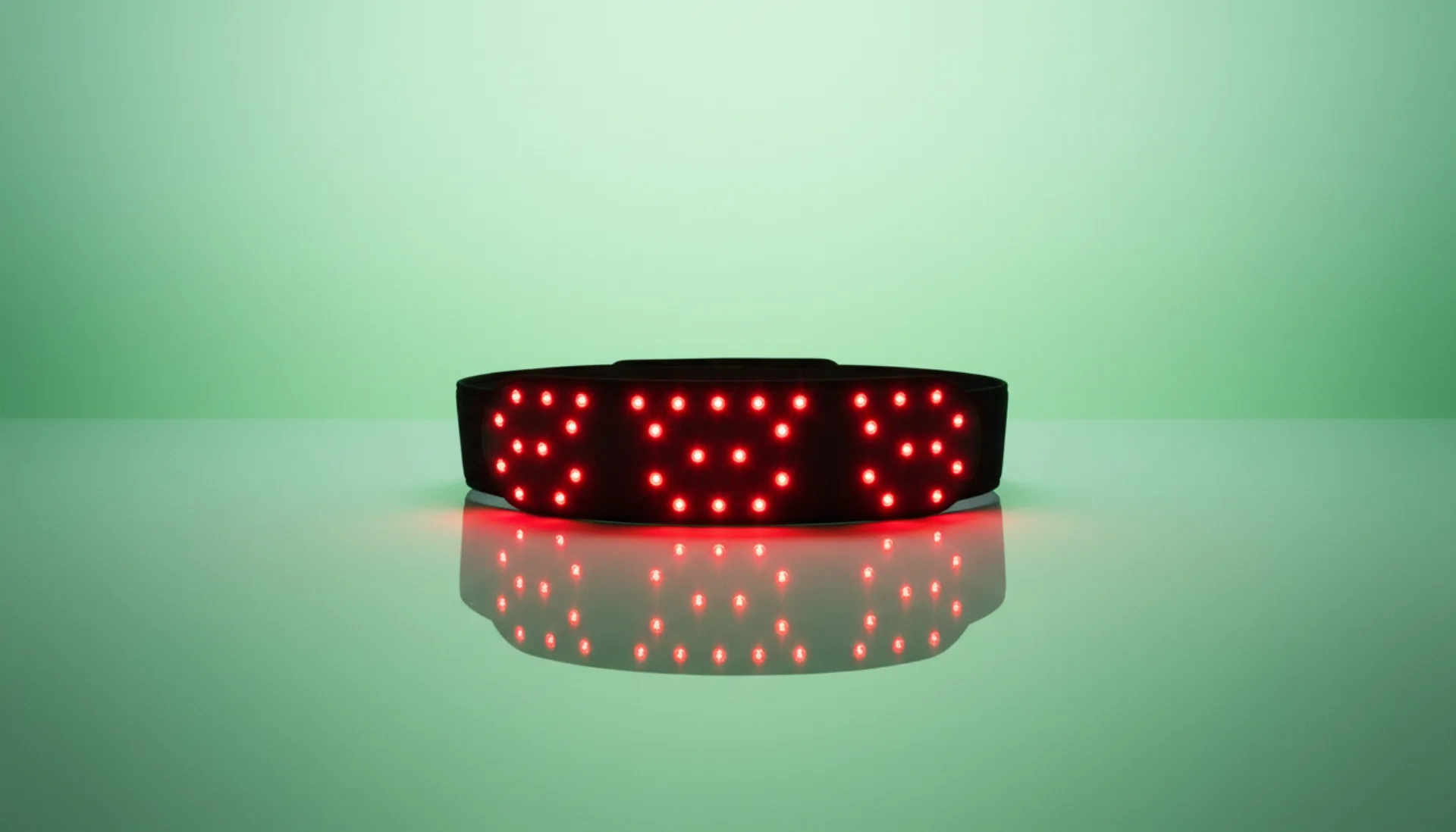 The Restoration Belt glowing red on a pale-green reflective studio surface